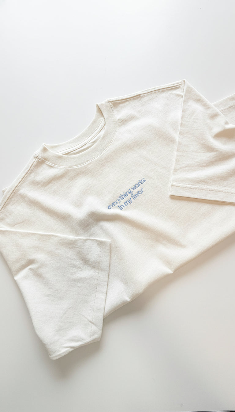 White t-shirt with blue text "everything works in my favor" on a white background