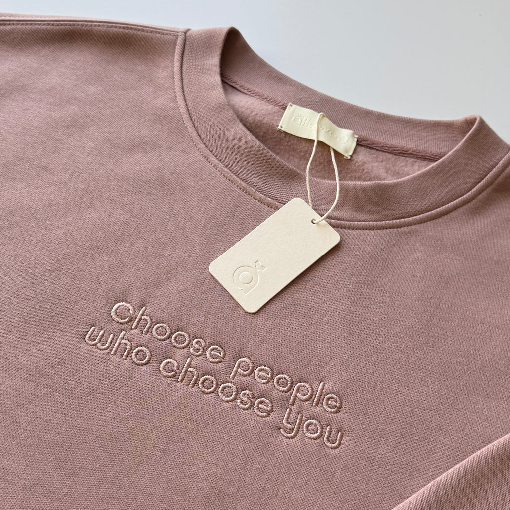 Pink-brown color sweatshirt with embroidered custom message "Choose people who choose you" on the chest. Brand tag is attached to the sweatshirt and displays the brand logo.