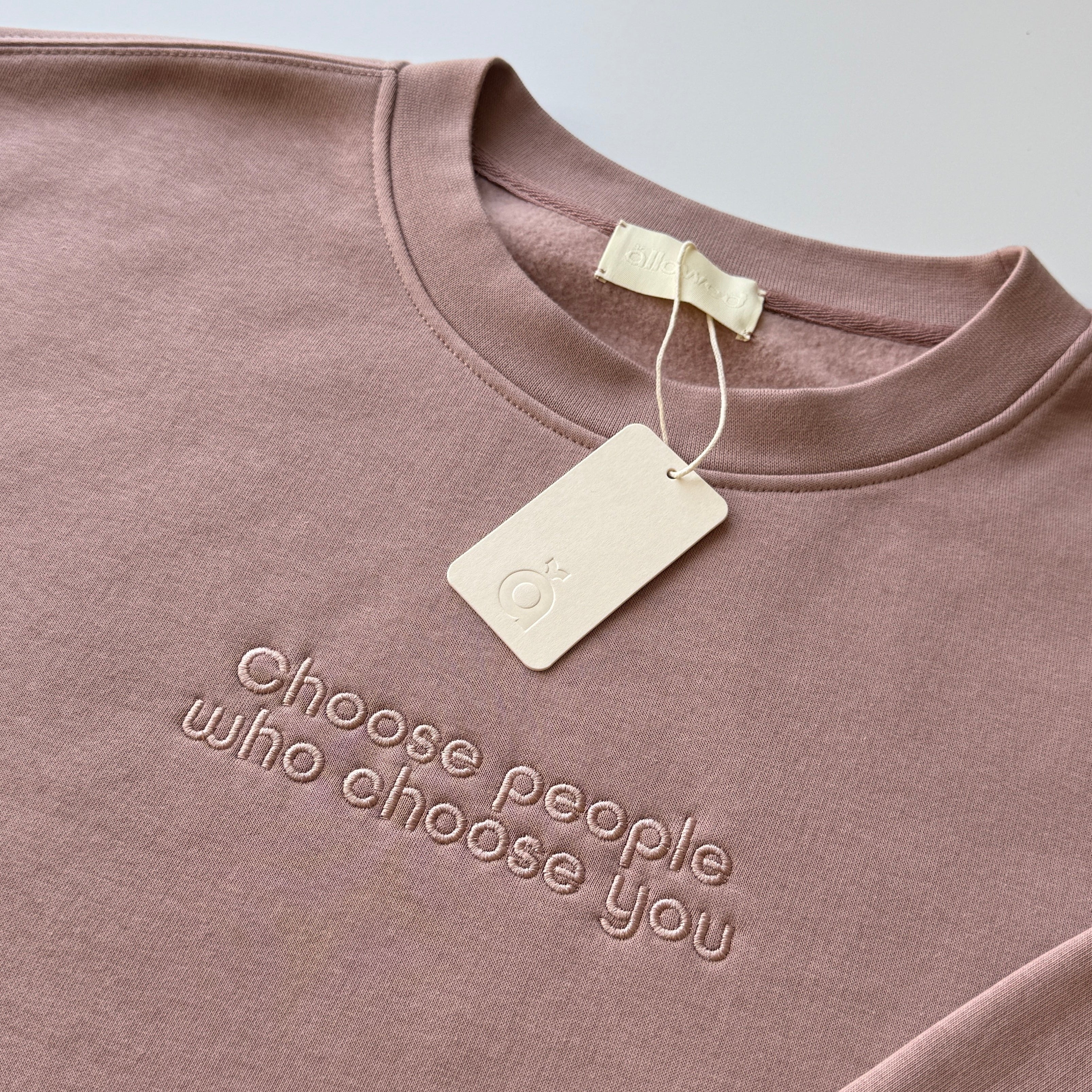 Pink-brown color sweatshirt with embroidered custom message "Choose people who choose you" on the chest. Brand tag is attached to the sweatshirt and displays the brand logo.