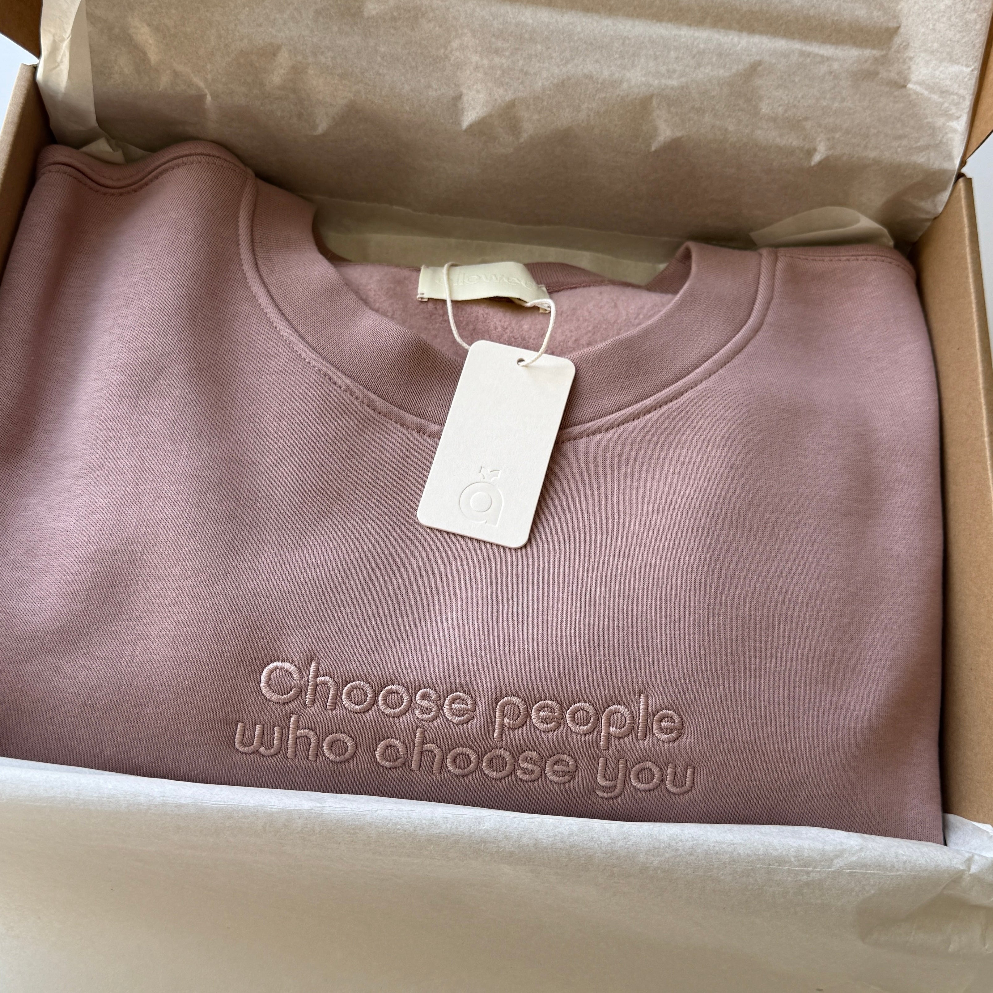 Pink sweatshirt with custom affirmation embroidered on the chest is packed and placed in the box